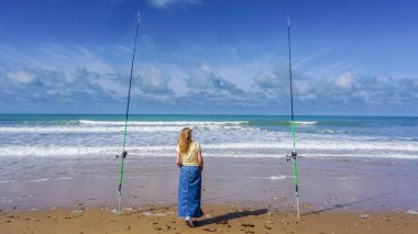 Yalnız bir kadın güzel bir güneş ve deniz gününde iki olta kamışı arasındaki denizi düşünür.