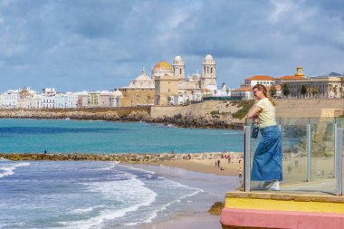 Bir kadın, güneşli bir günde deniz kıyısından gelen görkemli Cadiz Katedrali 'ni düşünüyor.