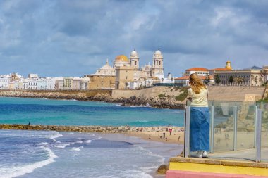 Bir kadın, güneşli bir günde deniz kıyısından gelen görkemli Cadiz Katedrali 'ni düşünüyor.