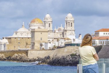 Bir kadın, güneşli bir günde deniz kıyısından gelen görkemli Cadiz Katedrali 'ni düşünüyor.