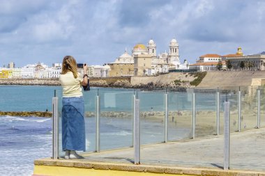 Bir kadın, güneşli bir günde deniz kıyısından gelen görkemli Cadiz Katedrali 'ni düşünüyor.