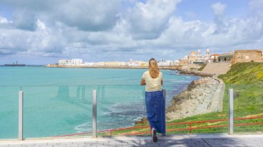 Bir kadın, güneşli bir günde deniz kıyısından gelen görkemli Cadiz Katedrali 'ni düşünüyor.