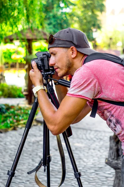 Genç adam fotoğrafçı Park doğa fotoğrafçılığı. siyah kamera bir tripod üzerinde. Peyzaj fotoğraf.