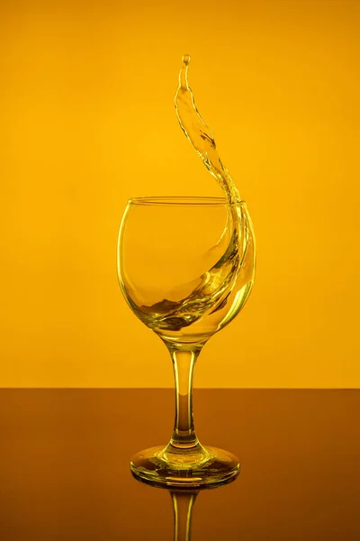 Splash of wine in a glass. Drink in glass on a yellow background.