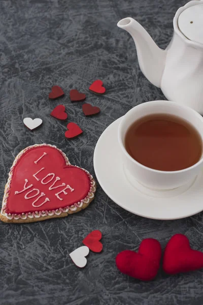 Romantic Valentine\'s Day breakfast. Heart-shaped cookie and a cup of tea on a gray table . Top view