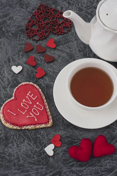 Romantic Valentine\'s Day breakfast. Heart-shaped cookie and a cup of tea on a gray table . Top view