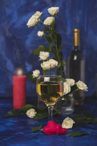 Valentine day. White wine. Romantic evening. A glass wine, a bunch of white roses and red hearts with smoke on a blue background. Holiday of lovers. A delicious alcoholic drink for two people.Picture.