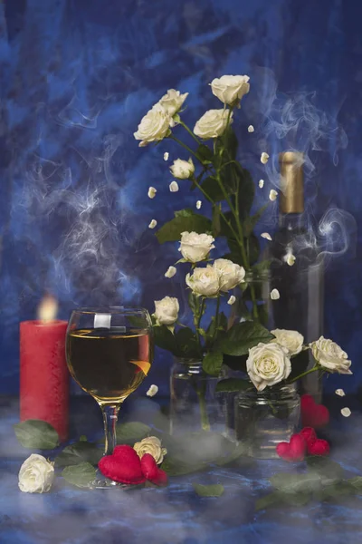 Valentine day. White wine. Romantic evening. Wine, a bunch of white roses and red hearts with smoke on a blue background. Holiday of lovers. A delicious alcoholic drink for two people.Picture magic