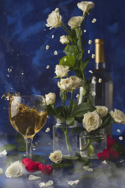 Valentines day.Splash of white wine. Romantic evening. Wine, a bunch of white roses and red hearts with smokeon a blue background. Holiday of lovers. A delicious alcoholic drink for two people.Picture