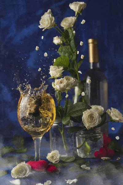 Valentines day.Splash of white wine. Romantic evening. Wine, a bunch of white roses and red hearts with smokeon a blue background. Holiday of lovers. A delicious alcoholic drink for two people.Picture magic.