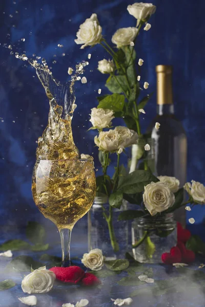 Valentines day.Splash of white wine. Romantic evening. Wine, a bunch of white roses and red hearts with smokeon a blue background. Holiday of lovers. A delicious alcoholic drink for two people.Picture magic.