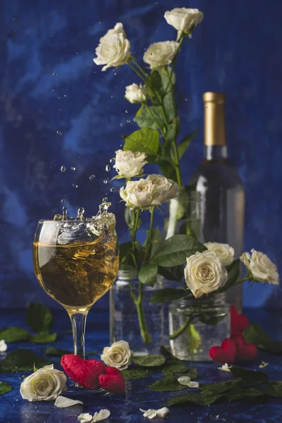 Valentines day. Splash of white wine. Romantic evening. Wine, a bunch of white roses and red hearts on a blue background. Holiday of lovers. A delicious alcoholic drink for two people. Picture photo.