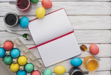Ahşap doku arka plan üzerinde renkli Paskalya yumurtaları. Beyaz ahşap masa için bir not defteri üzerinde renkli yumurta, boya, kaşık yemek tarifleri. Dini günün kutlu olsun insanlar için geleneksel. Üstten Görünüm. Kopya alanı.