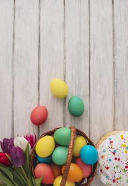 Renkli Paskalya yumurtaları, kek, Bahar Lale ahşap doku arka plan üzerinde. Bir beyaz tahta masada, renkli yumurta, çiçekler, ekmek. Dini günün kutlu olsun insanlar için geleneksel. Üstten Görünüm. Kopya alanı.
