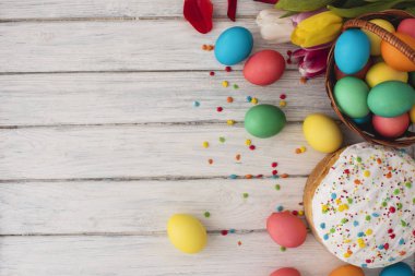 Renkli Paskalya yumurtaları, kek, Bahar Lale ahşap doku arka plan üzerinde. Bir beyaz tahta masada, renkli yumurta, çiçekler, ekmek. Dini günün kutlu olsun insanlar için geleneksel. Üstten Görünüm. Kopya alanı.