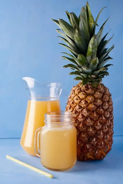 Pineapple juice and fresh tropical fruits  on a blue background. Sweet composition of summer drink.