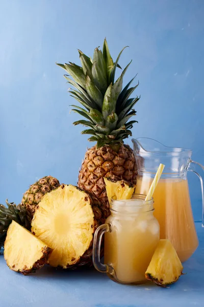 Pineapple juice and fresh tropical fruits  on a blue background. Sweet composition of summer drink.