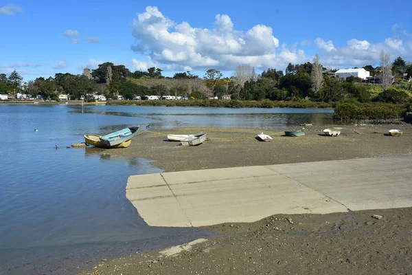 Small dinghies on mud flats next to concrete boat ramp in estuary at low tide.