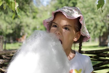 Adorable girl eating cotton candy at amusement park, summer vacation holidays, happy summertime concept  clipart