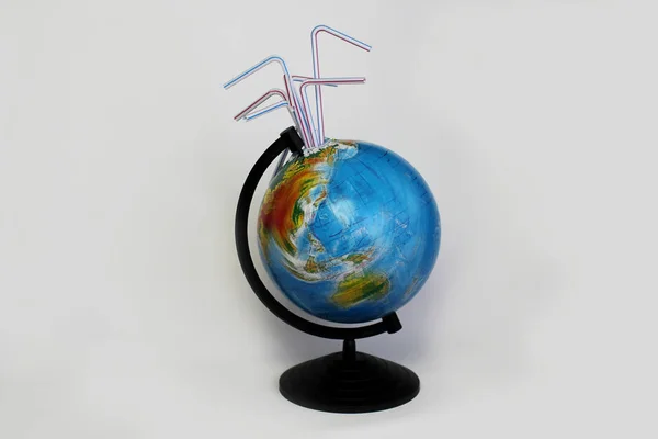 A globe of the earth in motion with cocktail plastic straws in it over white background, ecological problem concept, save water, do not suck the earth dry. Message for social advertising, place for inscription