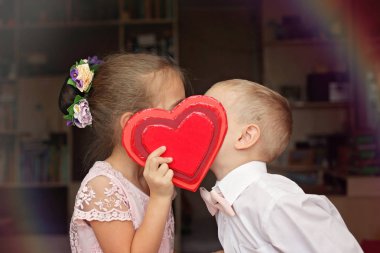 Beyaz gömlek ve yumuşak pembe papyon küçük çocuk ve güzel küçük prenses kırmızı bir kalp öpüşme yumuşak pembe elbise giymiş, onlar aşık, romantik ve kavramı, Sevgililer günü tebrik seviyorum