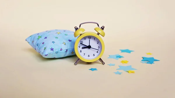 Reloj despertador amarillo y almohada azul claro — Foto de Stock