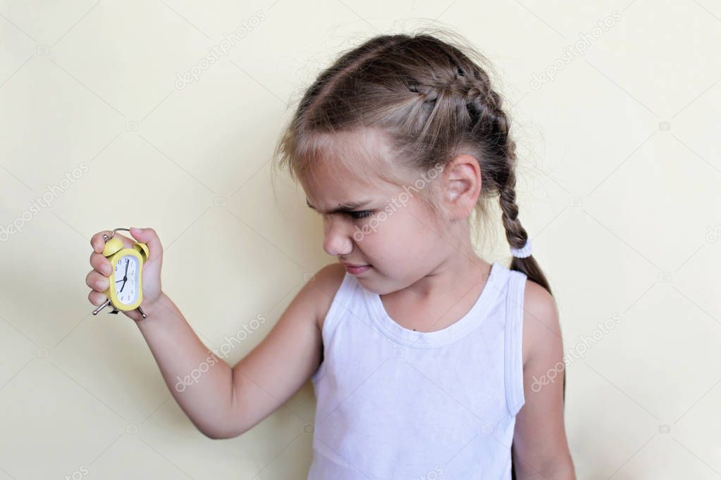 Sad pretty preschool girl holding a yellow alarm clock 
