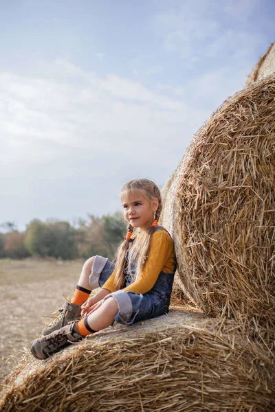 Linda chica divirtiéndose en rollos de pacas de heno en el campo — Foto de Stock
