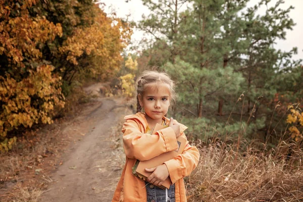 Smart cute kid girl holding a book with dry yellow leaves — Stock Photo, Image