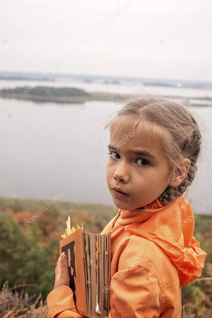 Smart cute kid girl holding a book with dry yellow leaves