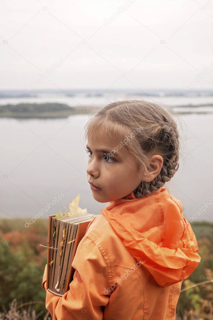 Smart cute kid girl holding a book with dry yellow leaves