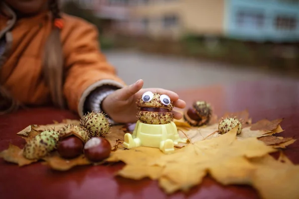 Осенние листья и каштан с игрушечными глазами на столе — стоковое фото