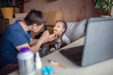 Orta yaşlı bir baba dizüstü bilgisayar ekranına bakıyor ve evdeki bir doktora danışıyor tecrit sırasında tele-sağlık hizmetleri, uzak video görüşmeleri, modern teknoloji sağlık uygulamaları...