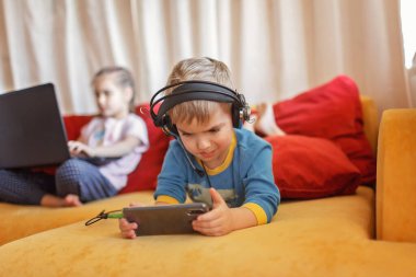 Gadget bağımlılığı, dijital yerli nesil alfa, tatlı çocuk kanepede uzanıyor ve sabahın erken saatlerinden kalma aletleri kullanıyor, online eğitim ve eğlence.