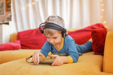 Gadget bağımlılığı, dijital yerli nesil alfa, tatlı çocuk kanepede uzanıyor ve sabahın erken saatlerinden kalma aletleri kullanıyor, online eğitim ve eğlence.