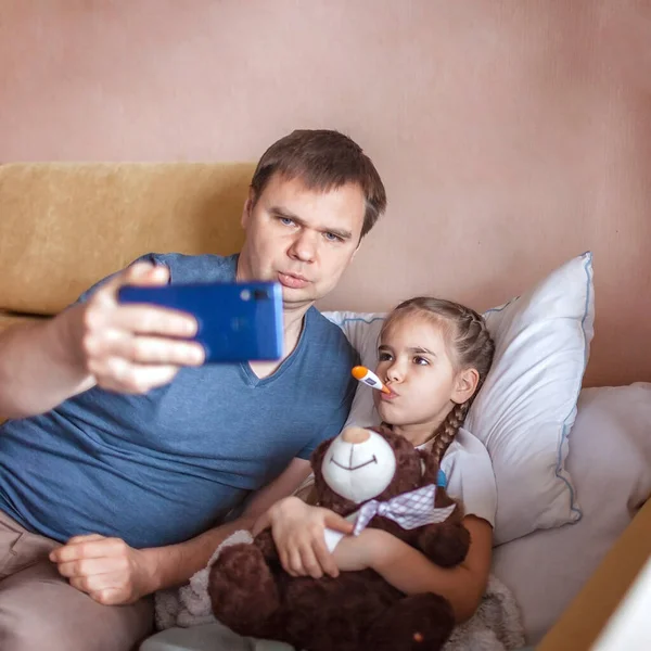 Middle-aged father looking at screen of smartphone and consulting with a doctor online at home, telehealth services during lockdown, distant video call, modern tech healthcare application