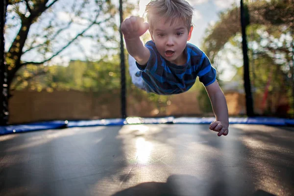 Cute little boy jumping on the trampoline like a superhero, he believes he can fly, summer family vacation. Outdoor fun and healthy activity, people enjoy life after lockdown