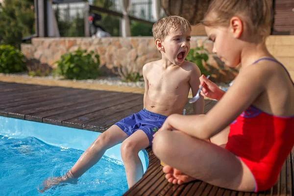 Family weekend in summer cottage, local staycation. Cute kids, boy and girl, have a fun and eating chocolate ice-cream near the swimming pool, happy summertime, outdoor lifestyle