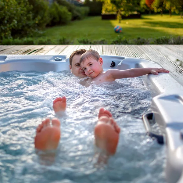 Family weekend in summer cottage, local staycation. Cute kid with father having rest together in bathtub with bubby water one hot day, happy summertime, outdoor lifestyle