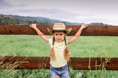 Yerel tatil, güvende kal, evde kal. Kovboy şapkalı küçük kız dağların arasındaki çiftlikte oynuyor, kırsalda mutlu bir yaz, çocukluk ve hayaller