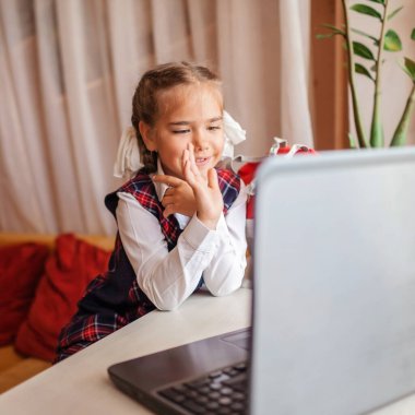 Okula dönmek, yeni normal eğitim. Okul üniformalı tatlı bir kız video görüşmesiyle birini selamlıyor ve yeni sırt çantasını gösteriyor. Sosyal uzaklık öğrenimi ve yeni rehberlik
