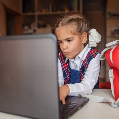 Okula dönmek, yeni normal eğitim. Okul üniformalı hoş bir kız internetten ders hazırlamak için sırt çantasından defter çıkarıyor. Sosyal uzaklık öğrenimi ve yeni rehberlik