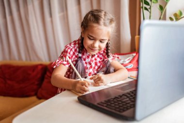 Uzaktan eğitim, okula dönüş konsepti. Evde online dersi sırasında ödev okuyan sevimli bir okul çocuğu, karantina sırasındaki sosyal uzaklık, kendini izole etme, internet üzerinden iletişim