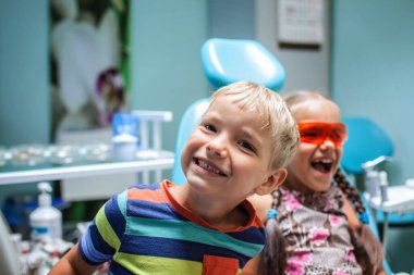 Two kids having fun and wearing medical eyeglasses during their visit to dentist office, the two are not scared. Healthy teeth and painless treatment, pediatric dentistry concept clipart