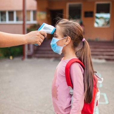 Okula geri döndüm. Sıcaklığı ölçen, temassız termometreyle maske takan bir öğretmen. Dikkatli olun, Coronavirus kilitlendikten sonra yeni okul rehberliği.