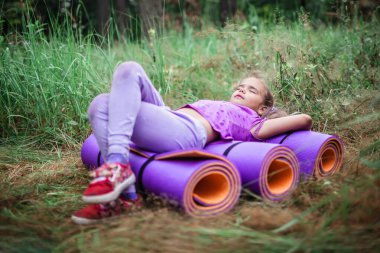 Active healthy weekend. Happy kid having rest and fun on the purple yoga mat during their hiking in the forest, local travel. Staycation in new normal life. Summer outdoor lifestyle clipart