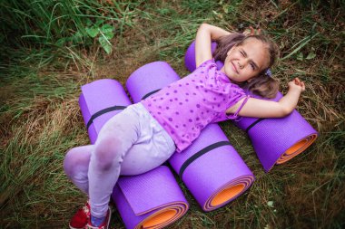Active healthy weekend. Happy kid having rest and fun on the purple yoga mat during their hiking in the forest, local travel. Staycation in new normal life. Summer outdoor lifestyle clipart