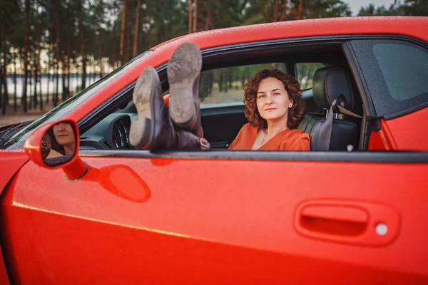 Autumn road trip, freedom and solo traveler. Pretty woman sitting in car on the bank of sea, feet on car window, looking at beautiful sunset after rain, drops on windshield, fall outdoor lifestyle