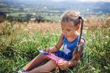 Patriot ve Ulusal Bayrak Günü kutlamaları. Küçük sevimli vatansever çayırda oturuyor ve mavi gökyüzü arka planında Birleşik Devletler bayrağını tutuyor.