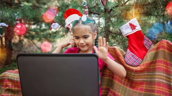 New normal online Christmas celebration. Cute sibling using laptop and festive fun props to celebrate Christmas with family via video chat, happy holidays, outdoor